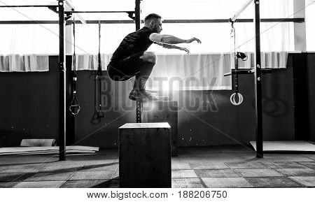 Fit young man jumping onto a box as part of exercise routine. Man doing box jump in the gym. Athlete is performing box jumps