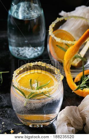 Tonic water cocktail with rosemary and orange. Two glasses and bottle with zest sugar and bubbles over black texture background. Refreshing beverage alco non alcohol. Close up