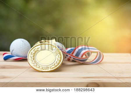 old gold medal and golf ball on wood in morning soft background Winner concept