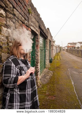 A mature woman smokes an electronic cigarette outside in poor weather conditions