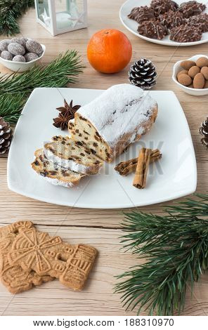 Arrangement of Gingerbread Spiced Biscuits and Mini Christstollen on light wooden background surrounded by Christmas decoration.