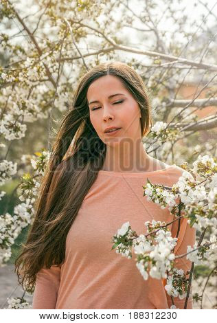 Romantic girl closeup face with close eyes, cherry blossom on the background. Pretty young woman dreaming about something closing eyes, spring time, sinny day.