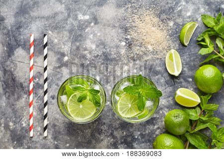Mojito cocktail traditional alcohol bar drink top view copy space two highball glass, summer tropical vacation beverage with rum, citrus slice, mint, lime juice, soda water and ice on concrete table.