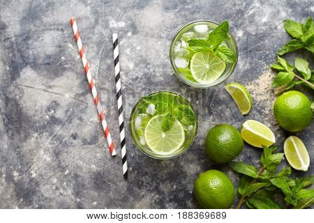 Mojito cocktail traditional Cuba travel vacation drink with rum, ice, mint, lime slices in highball glass on concrete table background, top view