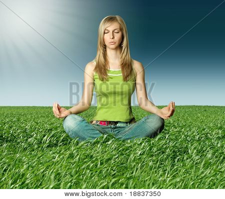 Blonde en lotus de poser dans l'herbe verte sur le ciel bleu