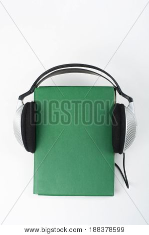 Audiobook on white background. Headphones put over green hardback book, empty cover, copy space for ad text. Distance education, e-learning concept