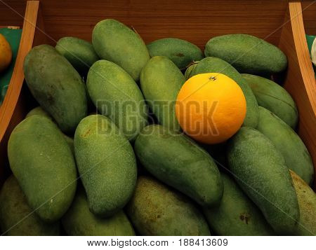The Only Orange Among a Pile of Mangoes