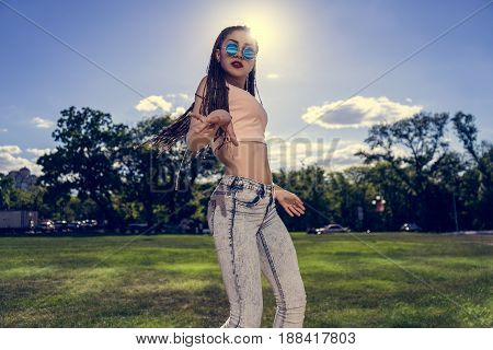 carefree girl with zizi cornrows dreadlocks dancing in the sunset on green grass of lawn. Free dancing