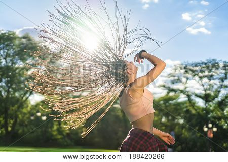 Happy carefree girl with zizi cornrows dreadlocks with hair up into air dancing in the sunset on green grass of lawn. Dancer girl