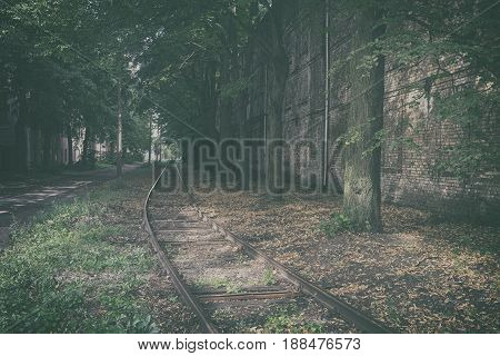 Mystical landscape with lost rails amidst a tree lane along a brick wall in the city of Riga