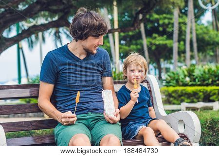 Father And Son Eat Fried Sweet Potatoes In The Park. Junk Food Concept