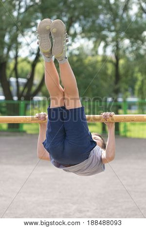 A Teenager In A T-shirt Is Engaged In Gymnastics On A Horizontal Bar