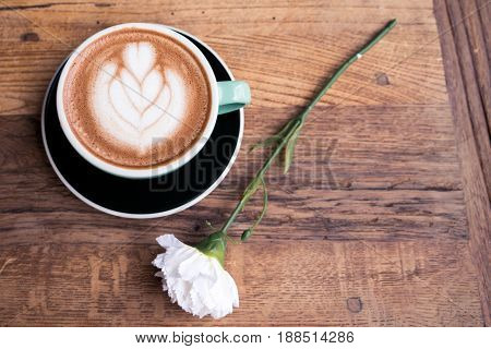 Hot mocha coffee or capuchino with heart pattern and white carnation flower on the wooden table