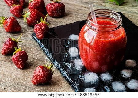 Strawberry smoothie with fresh berries and ice on a black stone board.