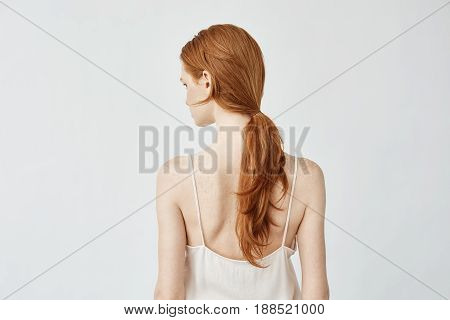 Portrait of young pretty girl with foxy hair posing standing back turning face to camera. Copy space. Isolated on white background.