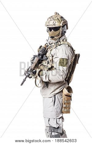 Army soldier in Protective Combat Uniform holding Special Operations Forces Combat Assault Rifle. Knee pads, mag recovery pouch, chest rig, military boots. Studio shot, isolated on white background