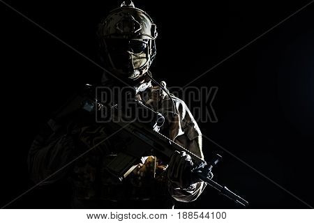 Army soldier in Protective Combat Uniform holding Special Operations Forces Combat Assault Rifle. Studio shot, dark contrast, cropped, black dark background, contour shot