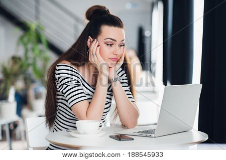 Disappointed lady sitting in a cafe during her lunch break and looking at laptop screen