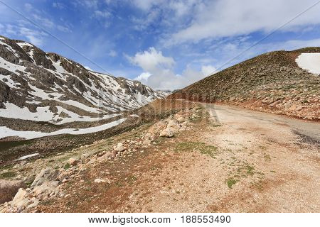 Mountain Landscape With Winding Road And Peaks Covered By Melting Snow Shot On Sunny Day