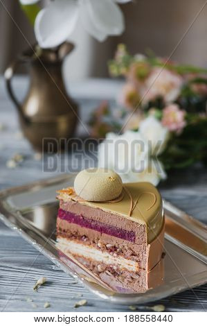 Bakery with piece of unusual yellow mousse cake with almond dacquoise, raspberry confit, crispy layer with caramelized hazelnuts and raspberry powder, mousse based on bitter chocolate served on wooden table.