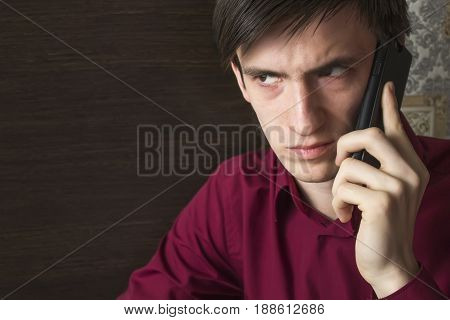 A young man in a purple shirt is waiting for an answer on a smartphone, with an alarming suspicious look, frowning