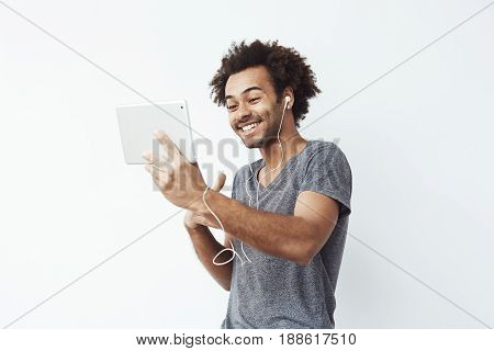 Funny african man in headphones laughing looking at tablet over white background. Copy space.