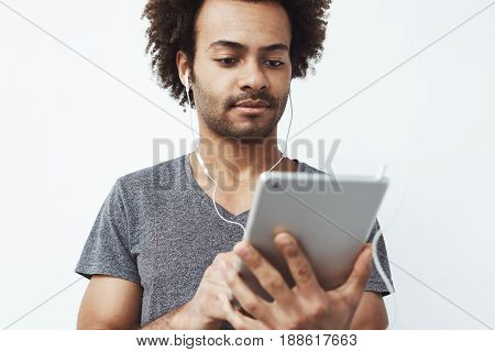 Young african man in headphones looking at tablet over white background. Copy space.