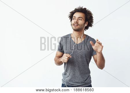 Cheerful african man listening to music in headphones dancing singing. White background. Copy space.
