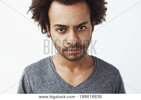 Close up photo of displeased african man looking at camera brutally. White background. Copy space.