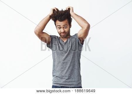 Surprised displeased african man looking down touching hair. White background. Copy space.