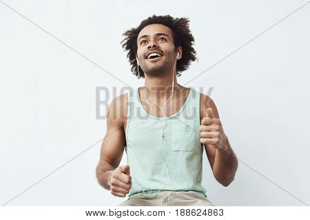 Young african man listening to music in headphones dancing over white background. Copy space.