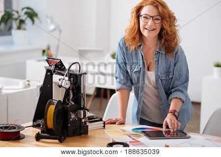 Great job. Happy cheerful nice woman standing at the table and smiling while being in a great mood