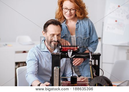 Out team. Delighted professional 3d designers smiling and looking at the 3d printer while working together