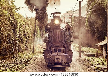 Steam narrow-gauge train moves from Yuejin to Shixi through the village. Jiayang Mining Region. Sichuan province. China.