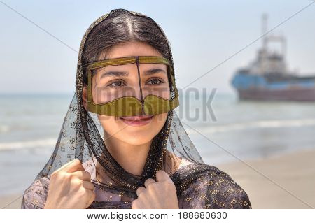 Young Iranian woman in traditional mask of Muslim women in southern Iran smiling standing on the shore of the Persian Gulf in Hormozgan province close-up portrait.