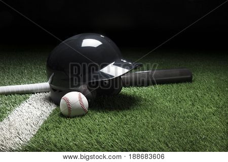 A baseball batting helmet bat and ball on a field with a white stripe and dark background