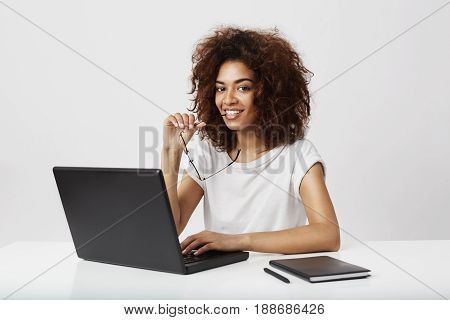 African girl smiling looking at camera sitting at wokplace with laptop. Copy space.