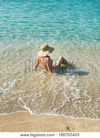 Beautiful slim senior woman tourist in bikini and hat sitting on sand enjoying clear sea waters at Meditteranean resort of Turkey in Alanya, Kleopatra beach