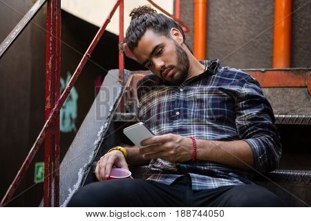 Man using mobile phone while having drink on staircase of bar