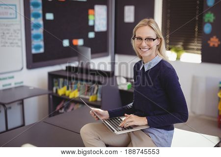 Portrait of happy teacher using laptop in classroom at school