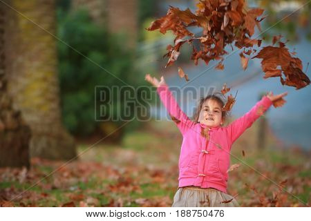 outdoor portrait of young happy child girl playing with autumn leaves in park on natural background