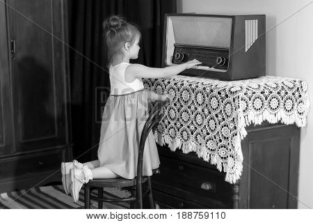 Curious little girl looking at a vintage radio . She is trying to push on the keys.Black-and-white photo. Retro style.