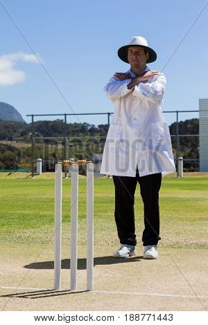 Full length of cricket umpire signaling cancel call sign during match against blue sky on sunny day