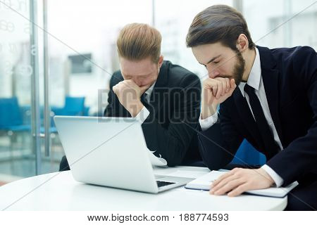 Stressed businessmen sitting by workplace in front of laptop