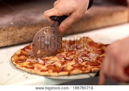 food, italian kitchen and cooking concept - cook hands with cutter cutting pizza to pieces at pizzeria