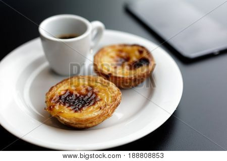 Portuguese egg tart pastry Pastel de nata on a plate with a cup of black coffee