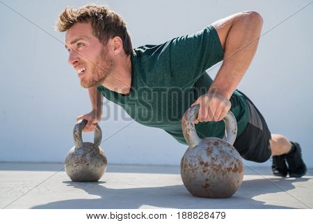 Fitness gym man doing pushups workout holding kettlebells for full extended push-ups floor exercises at outdoor gym. Athlete working out with bodyweight exercise.