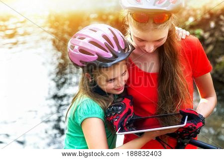 Bikes cycling girl. Children rides bicycle. Bicyclist girl watch on tablet computer. Kids looking for way. Dependence of adolescents on gadgets. Sports orienteering.