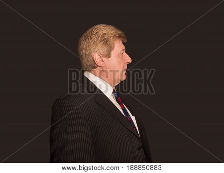 The profile of serious senior businessman looking at camera isolated on black studio background. Concept of business