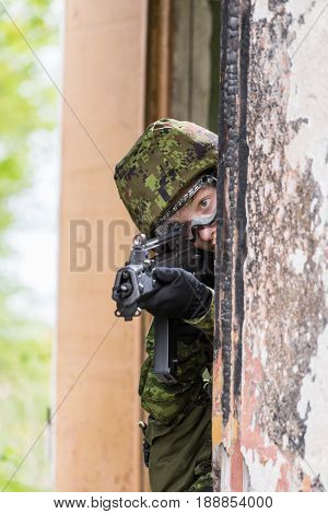 Portrait of armed woman with camouflage. Young female soldier observe with firearm. Child soldier with gun in war hearth house ruins background. Military army people concept